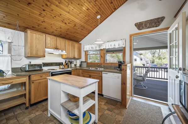 A kitchen with wooden cabinets, a white countertop, and a view of the outside through a glass door.