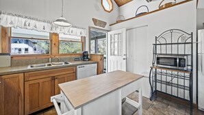 Una cocina con armarios de madera, un microondas integrado y una ventana con vistas a una zona residencial.