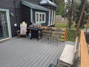 Een terras met een barbecue, stoelen en ski's die tegen een huis leunen.