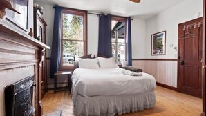 Een slaapkamer met een bed, een open haard, een raam met gordijnen, een deur en een kapstok.