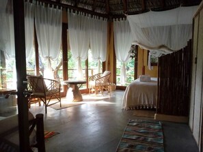 A room with a bed, two chairs, a table, and a window with curtains.