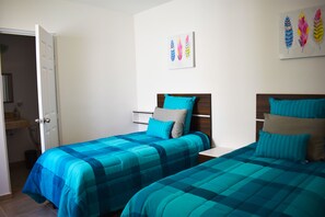 Ein Schlafzimmer mit zwei Betten, jeweils mit blaugrüner Bettwäsche, einem Holz-Kopfteil und einem Wandbild mit bunten Federn.