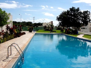 Ein rechteckiger Pool mit einer Metallleiter an einer Seite, umgeben von einer gefliesten Terrasse.