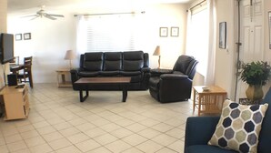A living room with a blue sofa, a black leather couch, a coffee table, and a ceiling fan. - Fantastic Vacation House on Private Lake in Fort Lauderdale (Fort Lauderdale)