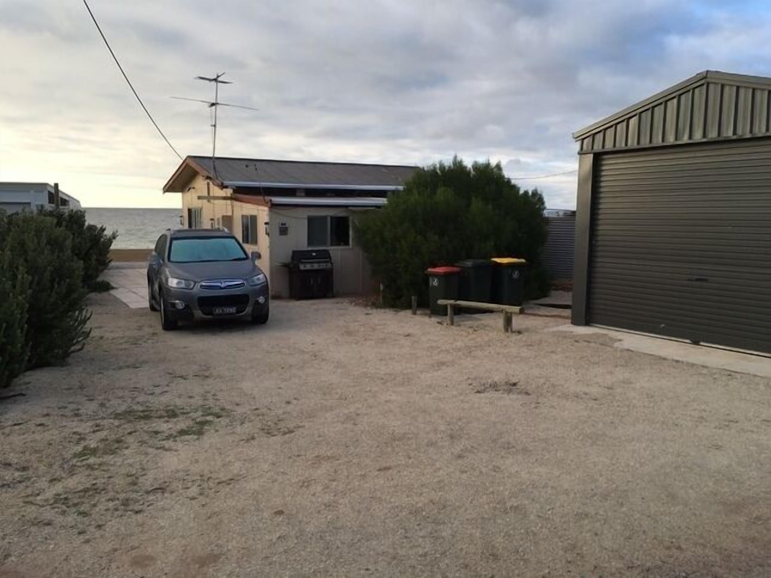 A residential property with a car parked in the driveway, a garage door, and a small building with a satellite dish.
