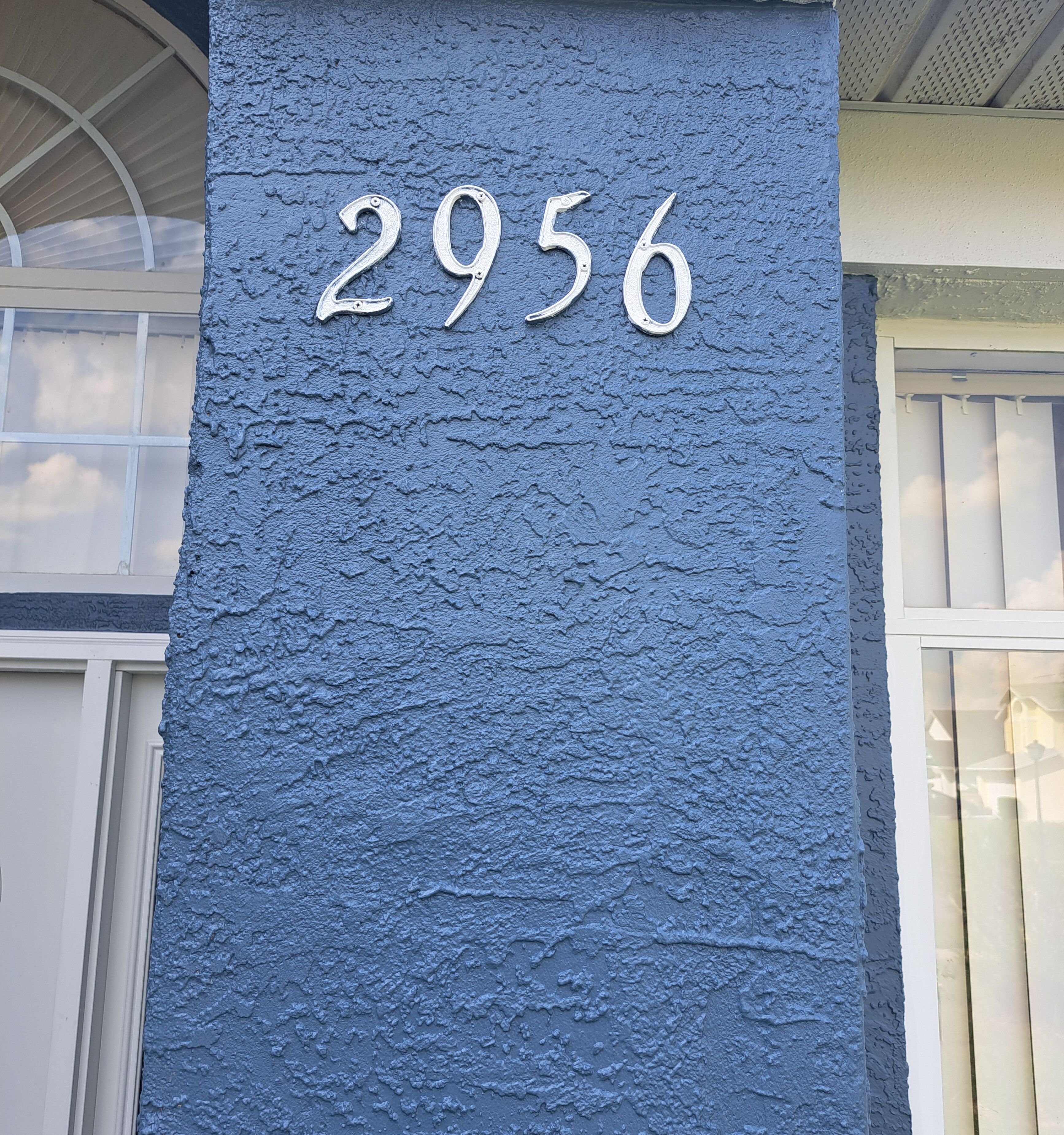 Un mur bleu à texture, sur lequel est gravé en relief le numéro 2956.
