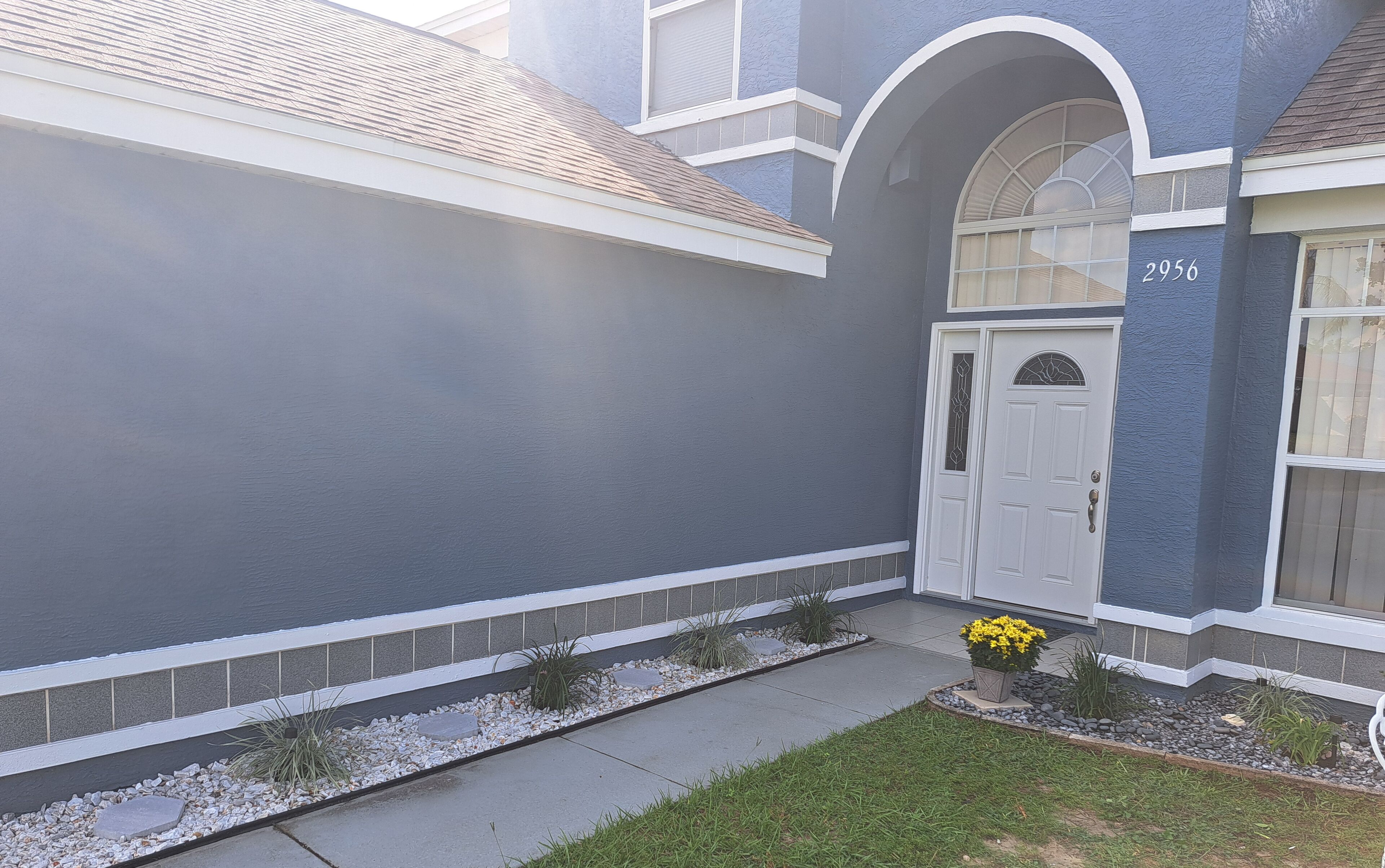 A residential building with a grey exterior, a white door, and a small garden area with yellow flowers.