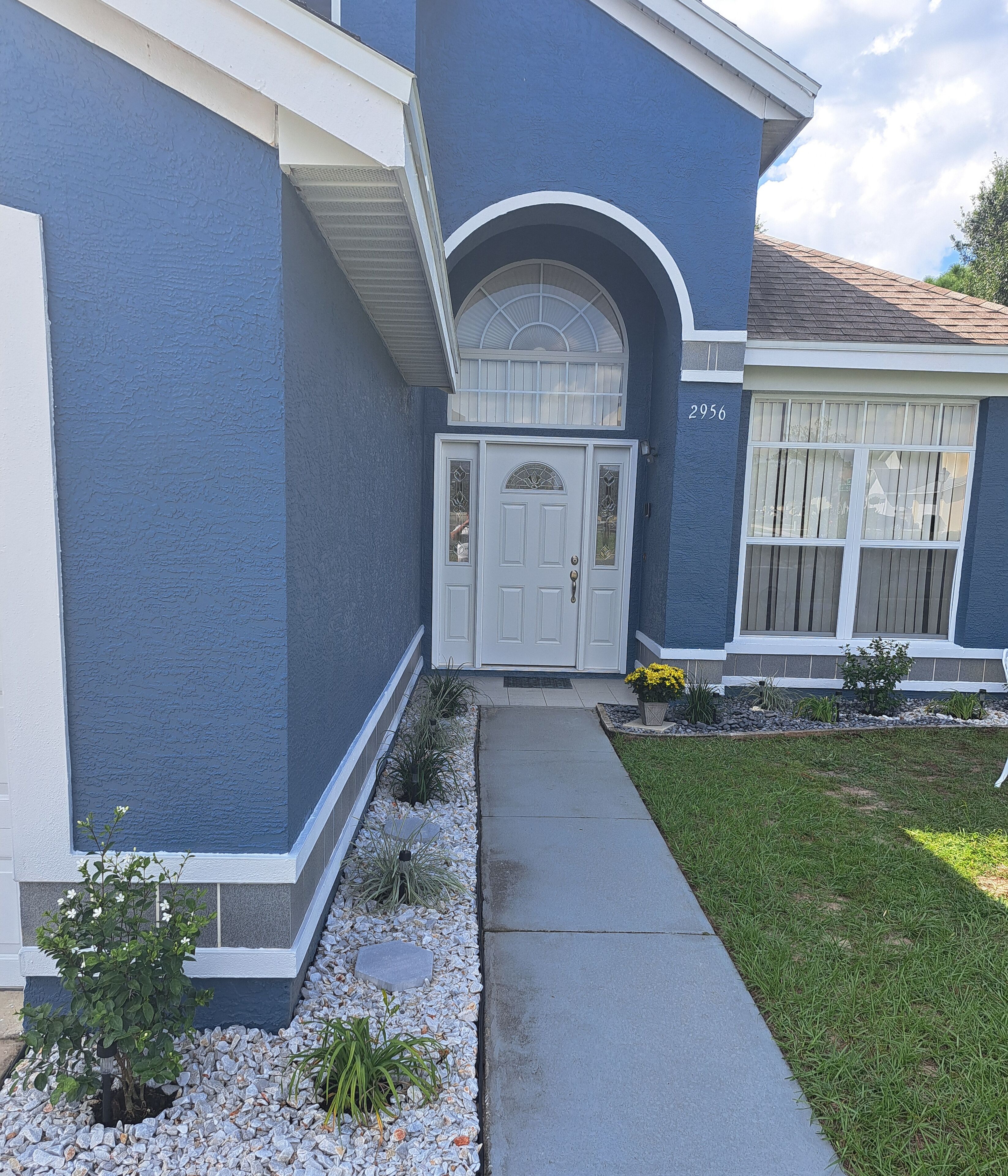 A residential house with a blue exterior, a white front door, and a number '2956' on the wall.