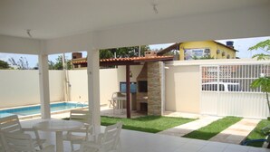 Un patio cubierto con piscina, sillas blancas y una zona de barbacoa de piedra.