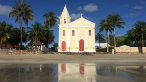 Una iglesia con un campanario y una cruz en la parte superior, rodeada de palmeras y una playa.
