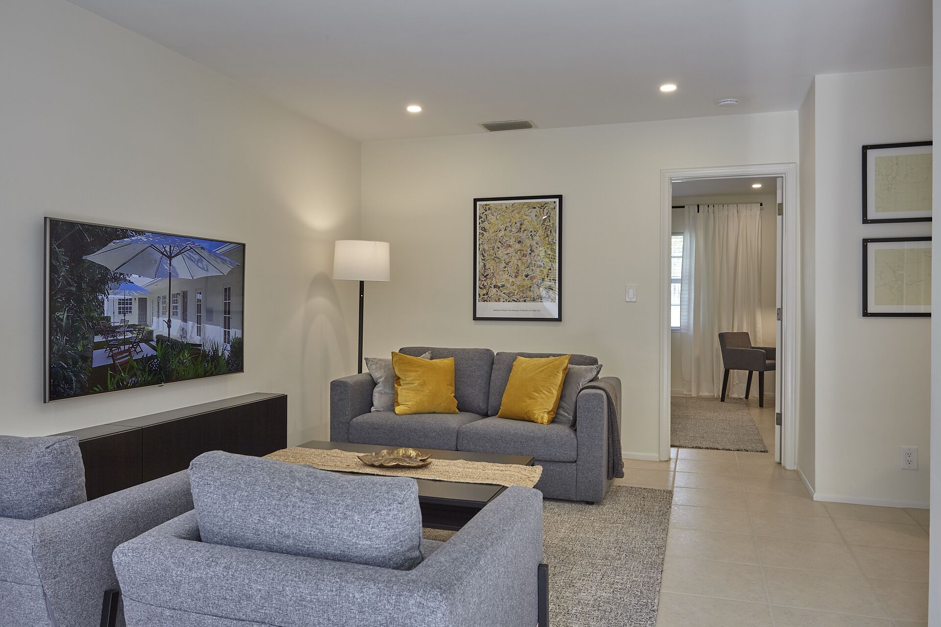 Een moderne woonkamer met grijze banken, een bijzettafeltje en een schilderij van een huis.