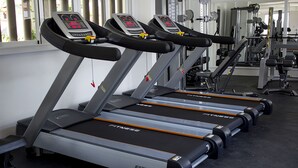 Tres cintas de correr en un gimnasio, con espejos y equipo de levantamiento de pesas al fondo.
