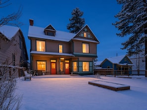 A two-story house with a snow-covered yard and a wooden deck. - Governor's Mansion Main — 4BR Sleeps 8, Pool Table, Sauna, Walk to Main St (Leadville)