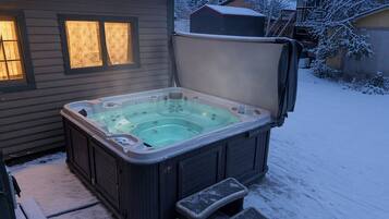 A hot tub with a cover, steps, and a house in the background.