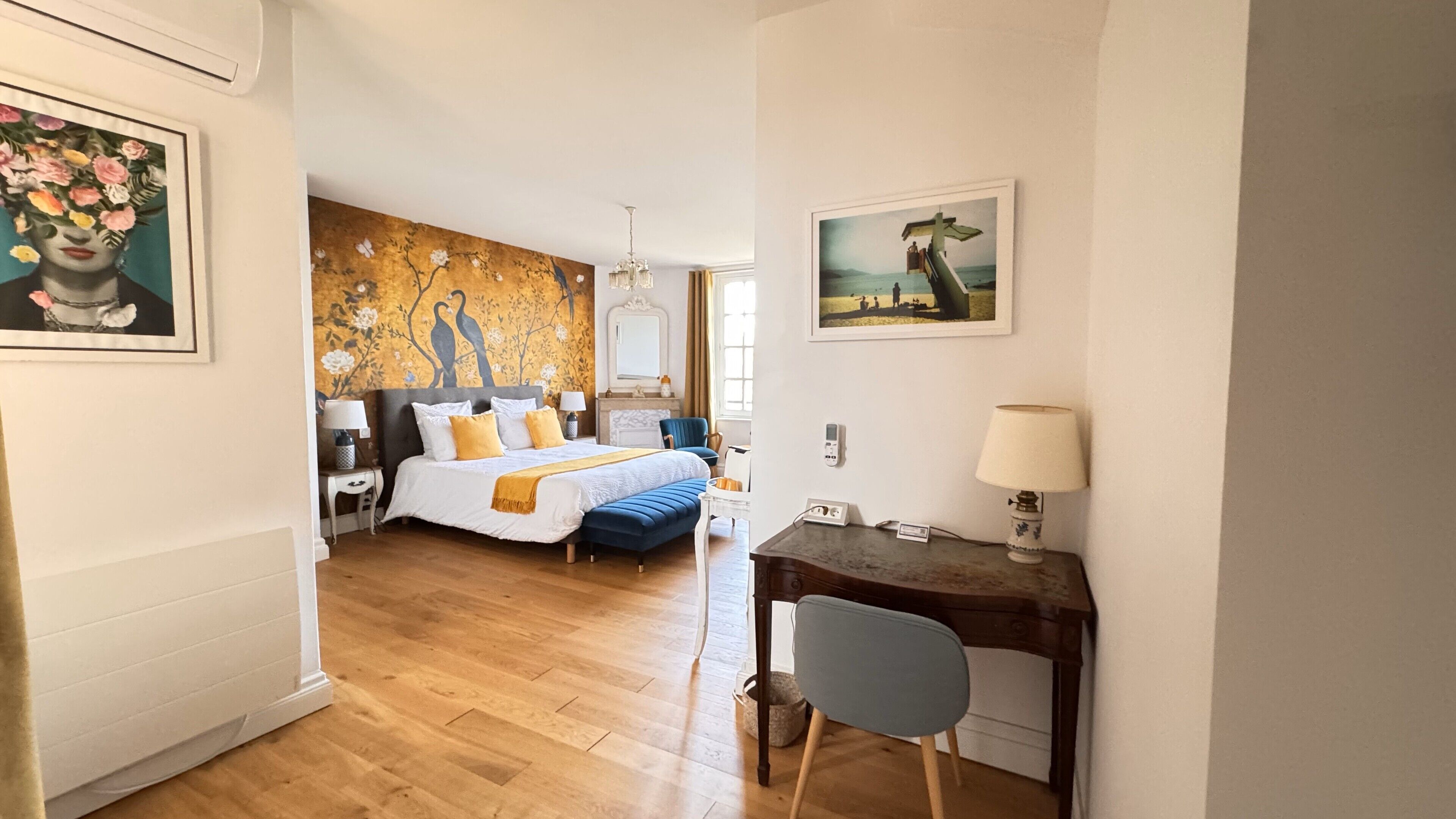 Une chambre d’hôtel équipée d’un lit, d’un bureau, d’une chaise, d’une lampe et d’œuvres d’art accrochées aux murs.