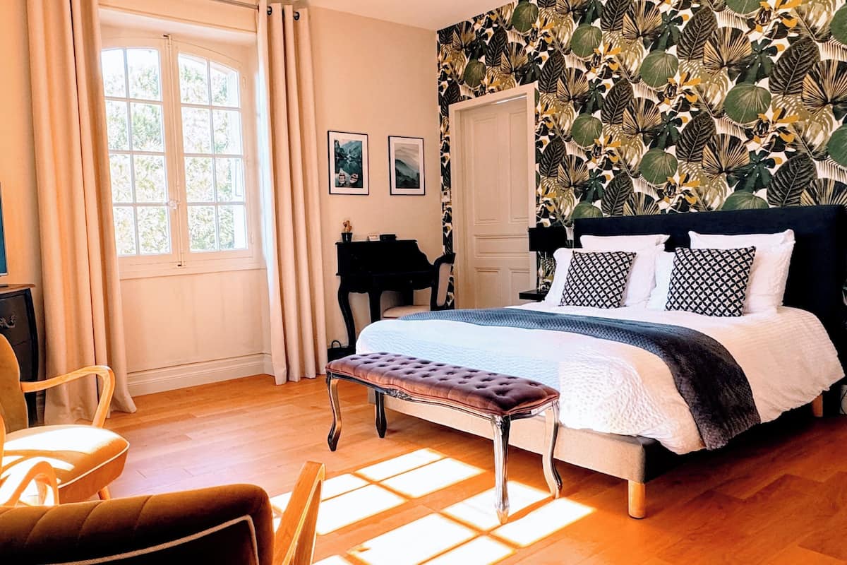 A bedroom with a bed, a chair, a desk, a television, and a window.