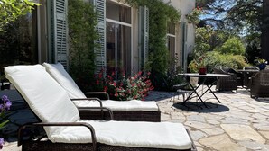 A patio with wicker lounge chairs, a stone-tiled floor, and a table with chairs. - Maison d'hôtes Le Parc (Labruguiere)