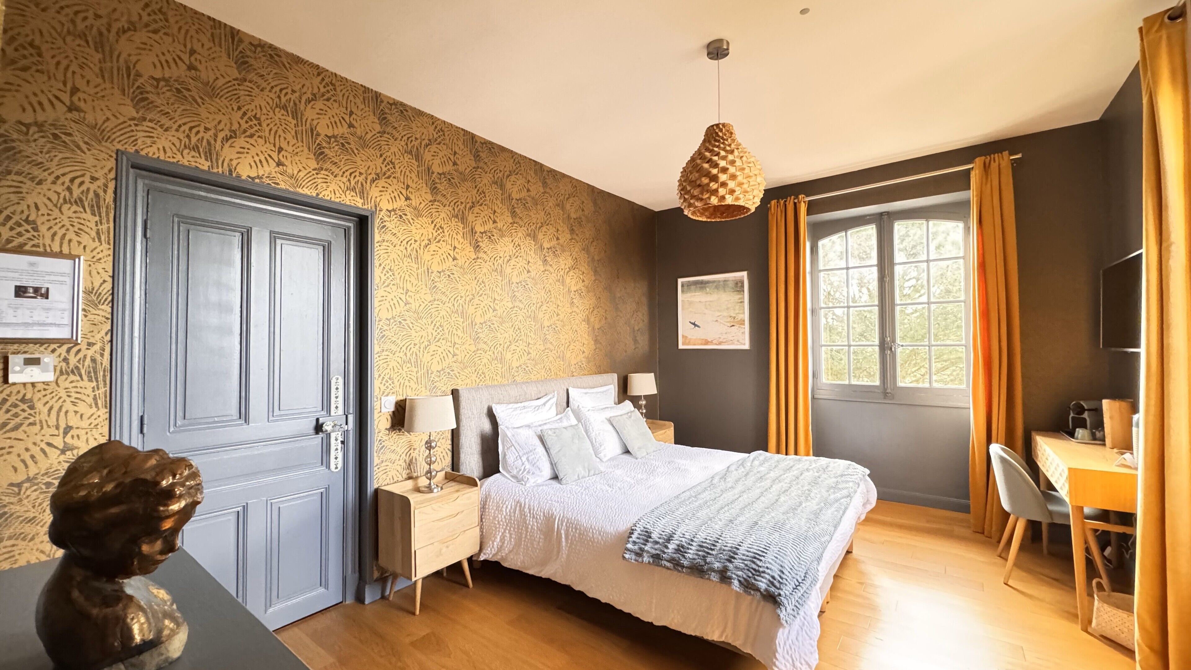 Un dormitorio con cama, mesitas de noche, escritorio y ventana con cortinas.