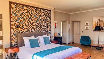 Una habitación de hotel con una cama grande, pared a cuadros, un escritorio con lámpara, una silla y una estantería.