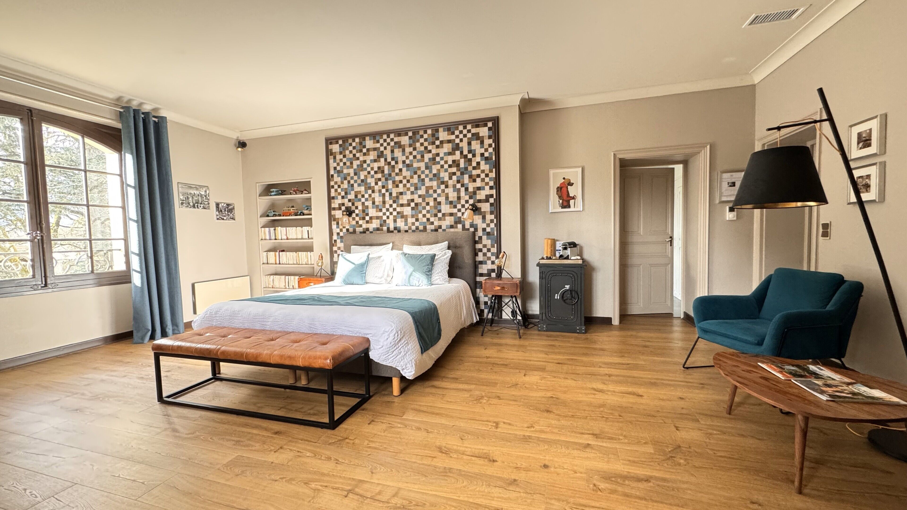 A bedroom with a bed, a bench, a chair, a desk, a bookshelf, and a door.
