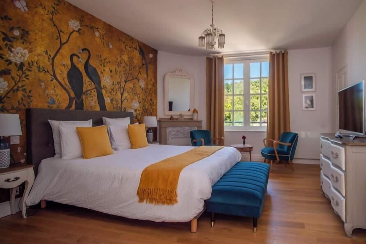 A bedroom with a large bed, a bench, a dresser, a television, and a window with curtains.