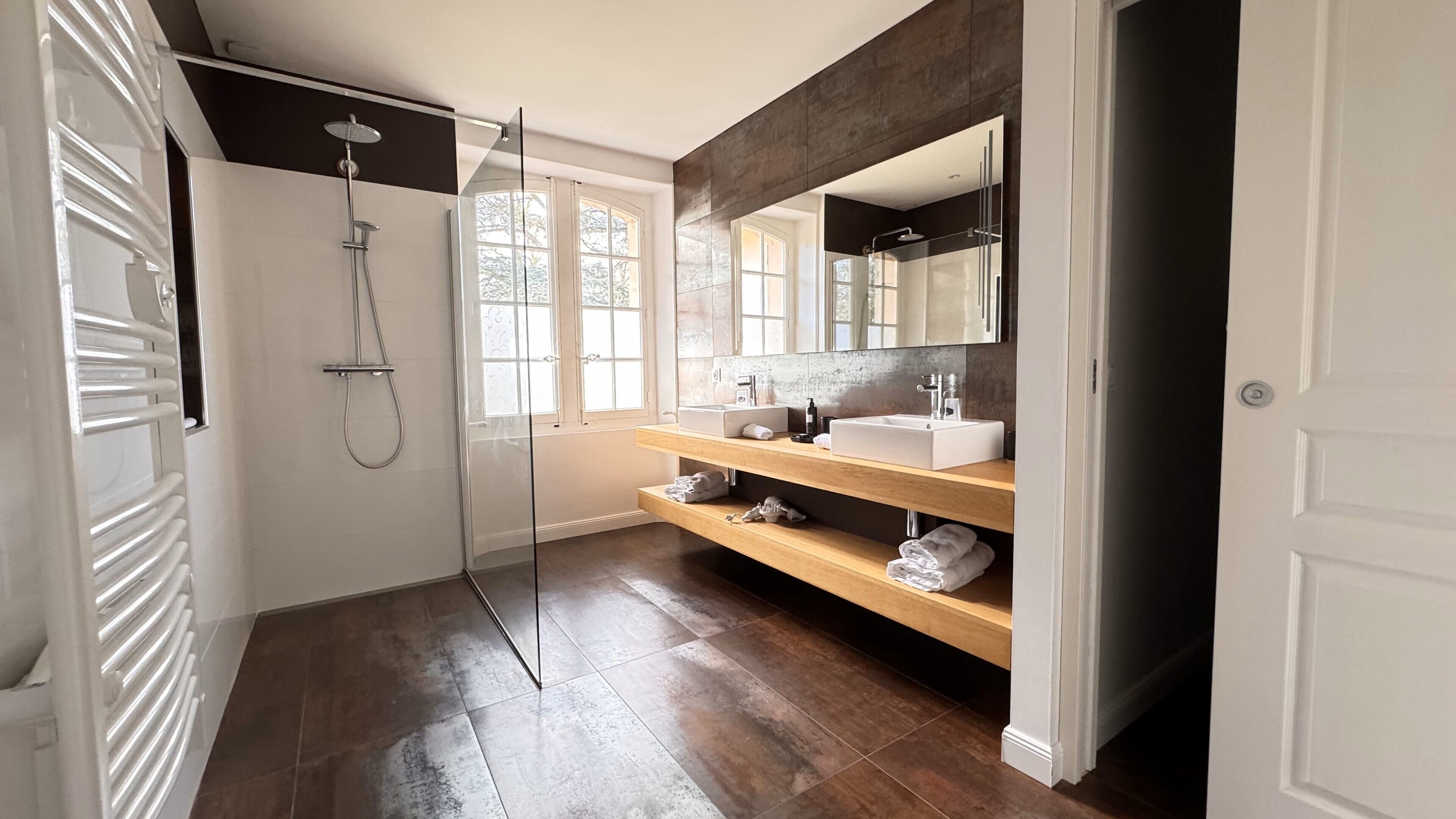 Een moderne badkamer met een douchecabine van glas, een wastafel met dubbele wastafels en een grote spiegel.