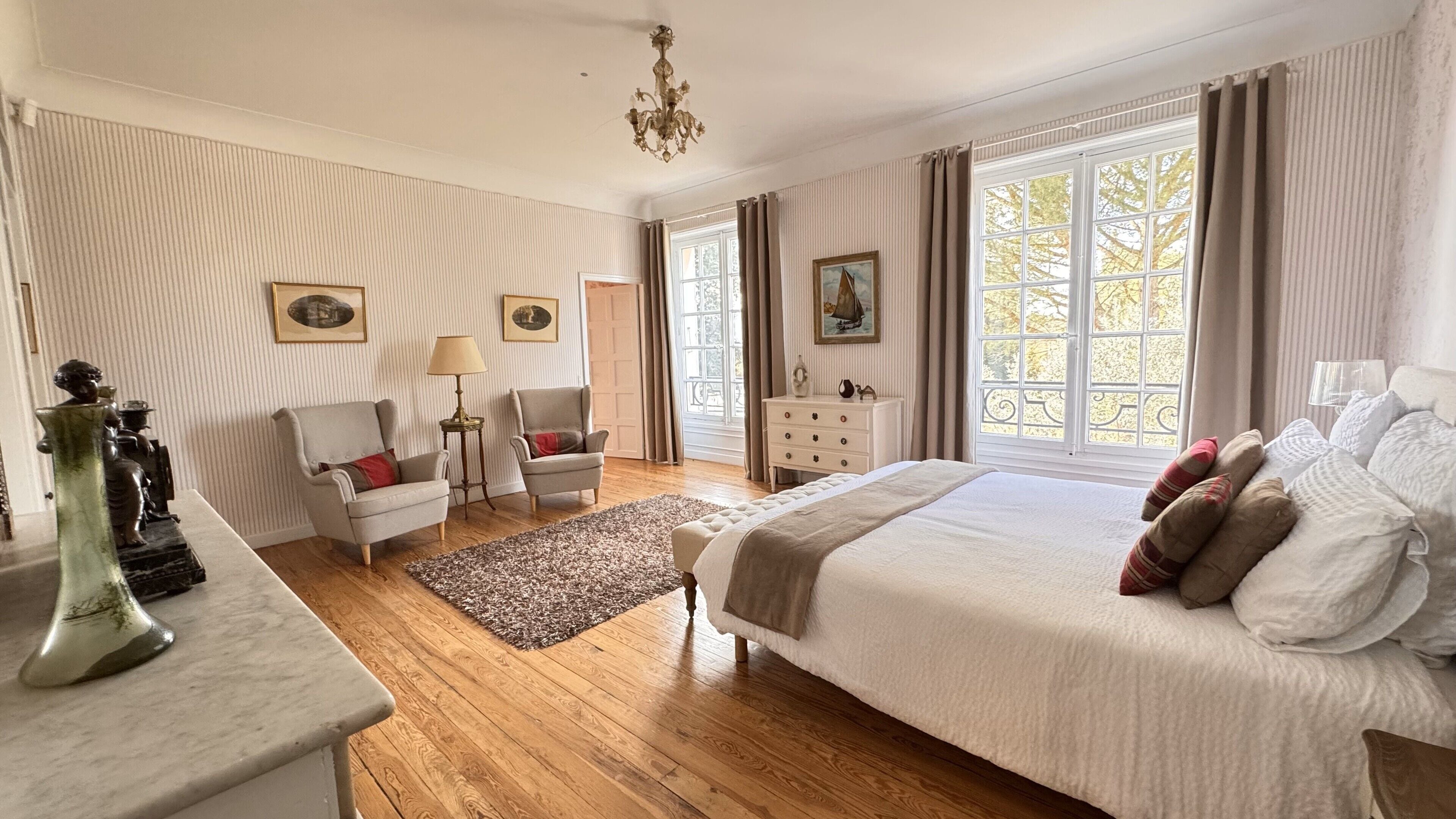 Un dormitorio amplio con una cama grande, dos sillones, un aparador y una araña.