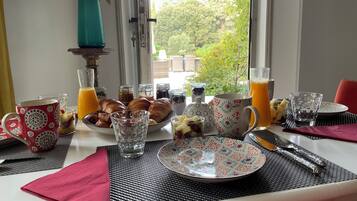 A breakfast table with pastries, fruit, and drinks, set near a window with a view of greenery.