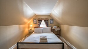Ein Schlafzimmer mit einem Bett, einem Nachttisch, einer Lampe, einem Fenster mit Vorhängen und gerahmten Bildern an der Wand.