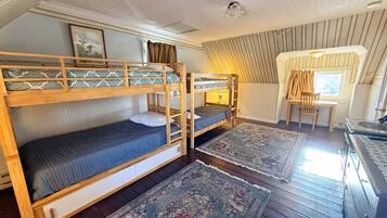 A room with bunk beds, a small desk, a chair, a window with curtains, and a radiator.