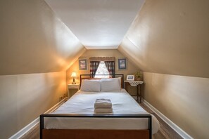 Une chambre à coucher avec un lit, une table de chevet, une lampe, une fenêtre avec des rideaux et des tableaux encadrés accrochés au mur.