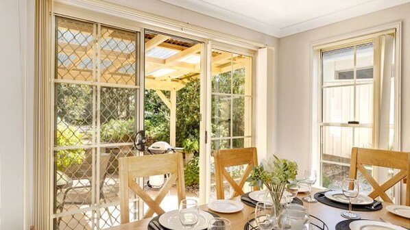 A dining area with a table set for four, large windows, and a view of greenery outside.