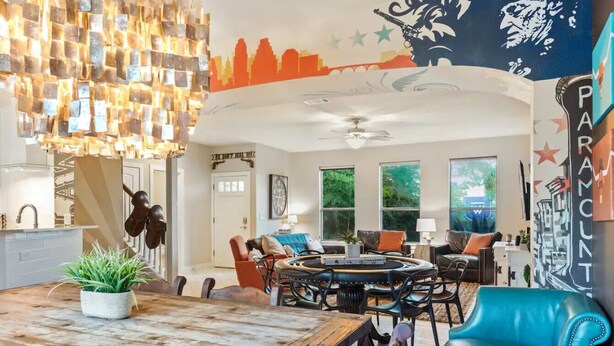 A modern living room with a wooden dining table, blue leather armchair, and a cityscape mural on the wall. - Single Malt Manor | Downtown Austin (Austin)