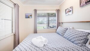 A hotel room with a bed, a ceiling fan, a window with blinds, and a painting on the wall.