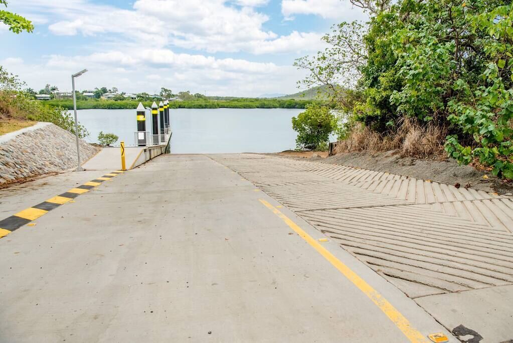 Un camí de formigó que condueix a un moll sobre un llac tranquil, envoltat de vegetació i un cel serè.