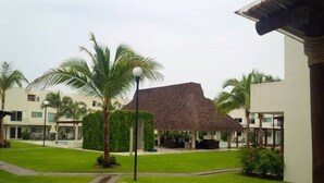 A resort with a thatched-roof structure, palm trees, and a well-maintained lawn. - Beautiful house in Acapulco Diamante, come and enjoy. Hermosa casa en Acapulco (Granjas del Marqués)