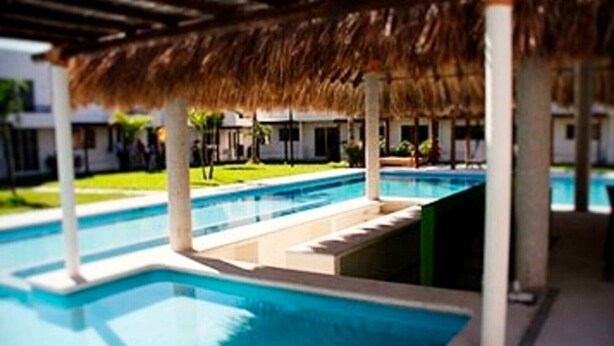 A swimming pool with a thatched roof structure, surrounded by a poolside area with steps leading into the water. - Beautiful house in Acapulco Diamante, come and enjoy. Hermosa casa en Acapulco (Granjas del Marqués)