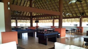 A spacious indoor area with a thatched roof, featuring multiple foosball tables, a pool table, and comfortable seating areas. - Beautiful house in Acapulco Diamante, come and enjoy. Hermosa casa en Acapulco (Granjas del Marqués)