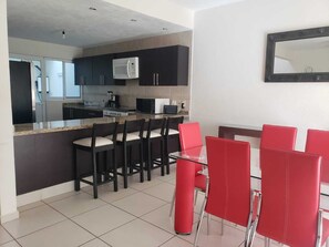 A modern kitchen with dark cabinets, a microwave, and a stove. There is a dining area with red chairs and a glass table.