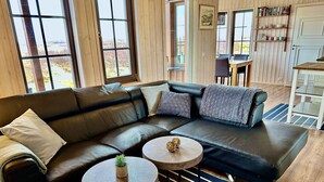 A modern living room with a black leather sectional sofa, two small round tables, and a view of the outdoors through large windows.
