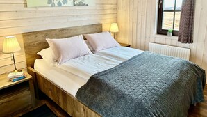 A wooden-paneled room with a bed, two bedside lamps, a radiator, and a window with curtains.