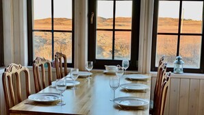 A dining table set for six with six chairs, large windows with a view of a hilly landscape, and a decorative lantern on the windowsill.