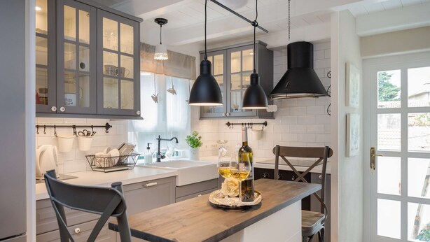 Una cocina con una isla de madera, luces colgantes y vistas a través de una puerta.