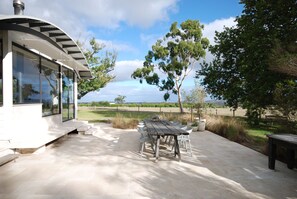 A modern outdoor patio with a dining table and chairs, a bench, and a glass-enclosed structure with a curved roof.