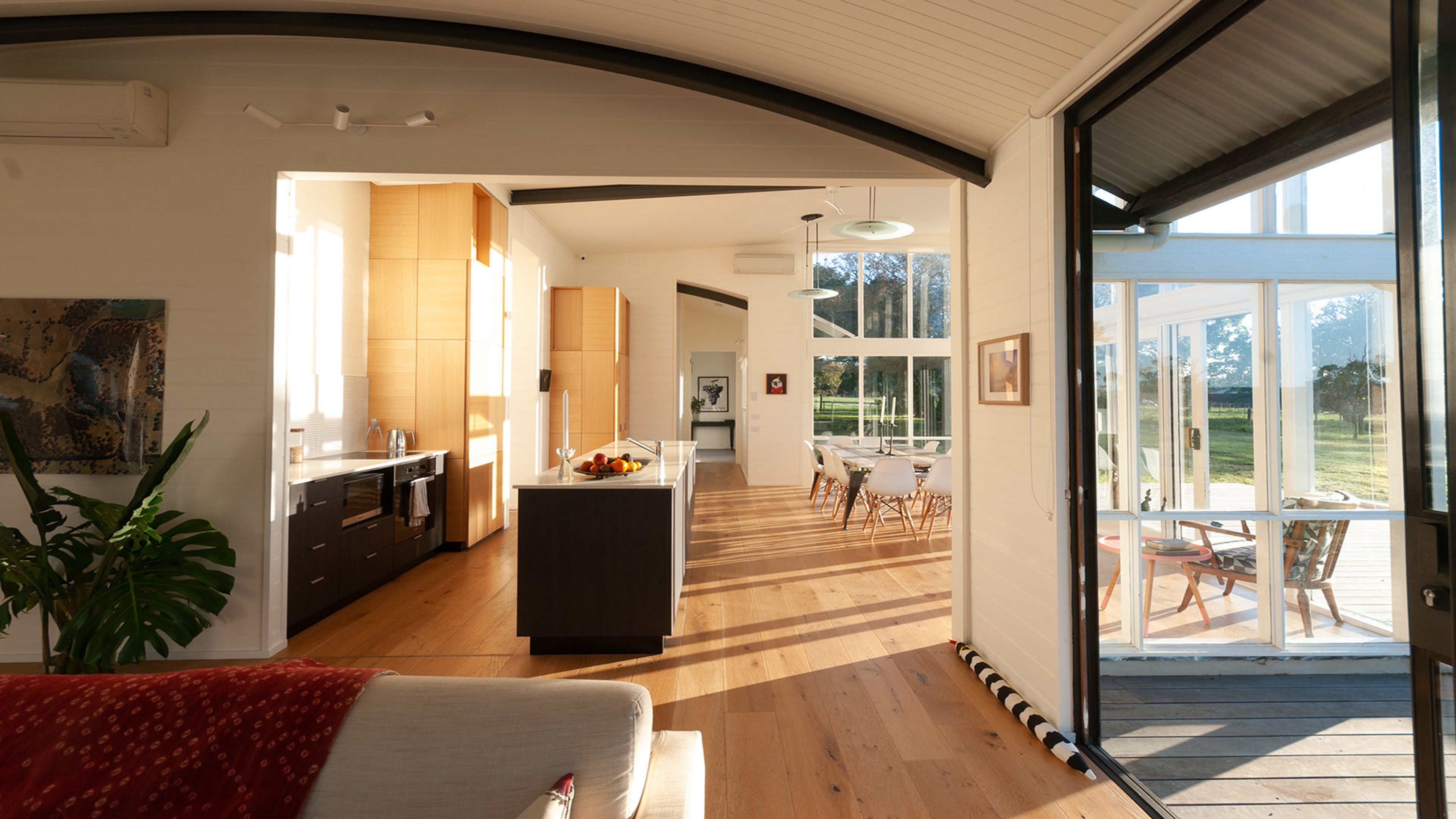A modern kitchen with wooden cabinets and a central island, a dining area with a table and chairs, and a large sliding glass door leading to an outdoor deck.