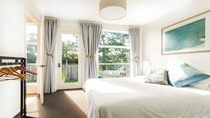 A bedroom with a bed, a window with curtains, a door leading outside, and a painting on the wall.