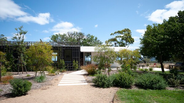 A modern building with a pathway leading to a covered area, surrounded by greenery and trees.