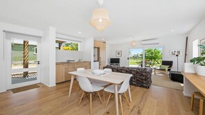 A modern kitchen with wooden cabinets, a dining area with a white table and chairs, and a view of the outdoors.