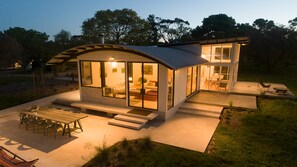 A modern house with a large glass facade, a patio with outdoor furniture, and a well-maintained lawn.