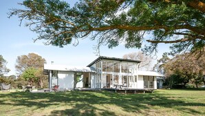 A modern house with a glass extension, surrounded by a grassy yard and trees.
